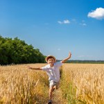 Happy boy with arms outstretched in a wheat field on a sunny day. Childhood, freedom, and summer concept