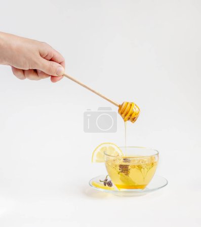 Hand tropft Honig auf eine Tasse Kräutertee, umgeben von Blumen und Flaschen. Konzept eines gesunden Lebensstils und natürlicher Heilmittel