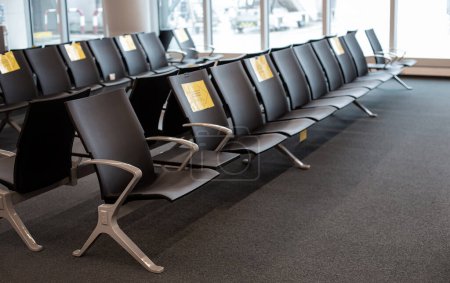Empty airport waiting area with rows of seats and yellow signs indicating social distancing, copy space