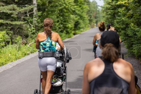 Téléchargez les photos : Photo de dos prise par maman instructrice marchant avec d'autres nouvelles mères dans une session de groupe de cardio et d'aérobic à l'extérieur - en image libre de droit