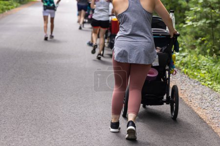 Photo for Photo taken from the backside of group of mothers walking outside in a natural environment with their babies inside the strollers - Royalty Free Image