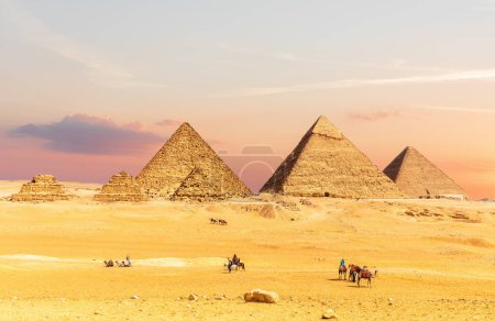 Foto de Pirámides de Egipto al atardecer con turistas cercanos, desierto de Giza, El Cairo. - Imagen libre de derechos
