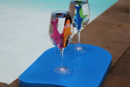 Foto de Pescado de goma en copas de vino de plástico en una bandeja azul junto a una piscina - Imagen libre de derechos