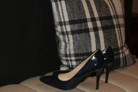 Foto de Zapatos de charol de tacón alto junto a almohada a cuadros en banco de cojín - Imagen libre de derechos