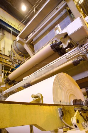 Grandes rollos de papel saliendo de la maquinaria en una fábrica de papel.