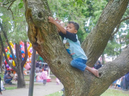 Téléchargez les photos : Malang, indonésie - 5 février 2023 : un garçon asiatique escalade un arbre en jouant. activités de plein air pour enfants qui nécessitent du courage - en image libre de droit