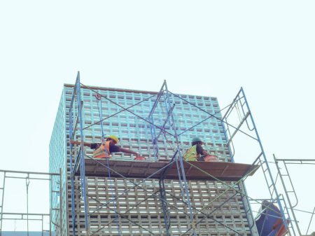 Photo for Malang, Indonesia - December 24, 2023 : construction workers are painting the side of a multi-storey building using an iron ladder structure - Royalty Free Image