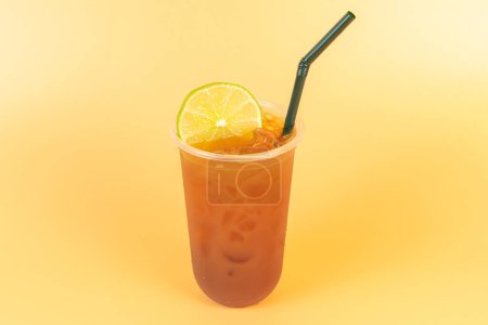 Kalter Brühtee oder schwarzer Tee mit Zitrone in einem Plastikglas auf orangefarbenem Hintergrund. Erfrischendes Getränk zur Abkühlung im Sommer.