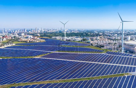 Foto de Paneles solares fotografiados desde el aire. En el fondo, palas de aerogeneradores y una ciudad de alta tecnología - Imagen libre de derechos
