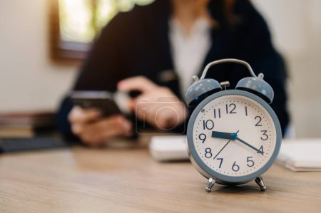 Photo for Alarm clock on wooden desk. Businesswoman working and using mobile phone - Royalty Free Image