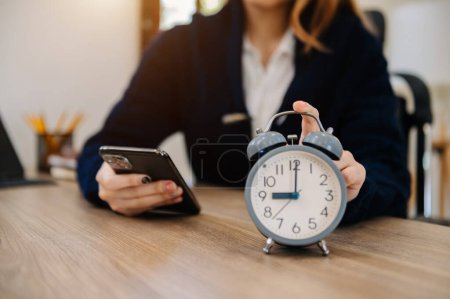 Photo for Alarm clock on the desk. Business working in office building or home at night using laptop. and smart phone - Royalty Free Image