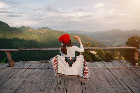 Foto de Rear view image of a female traveler sitting and holding breakfast looking at a beautiful mountain, field and nature view in sunlight - Imagen libre de derechos