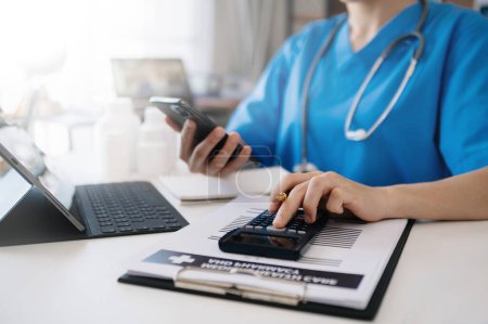 Foto de Healthcare costs and fees concept.Hands of smart doctor used a calculator and smartphone, tablet for medical costs at hospital in morning light - Imagen libre de derechos