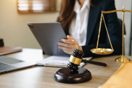 Téléchargez les photos : Woman lawyer in the office with brass scale and using tablet and laptop on wooden table. justice and law concept in morning light - en image libre de droit