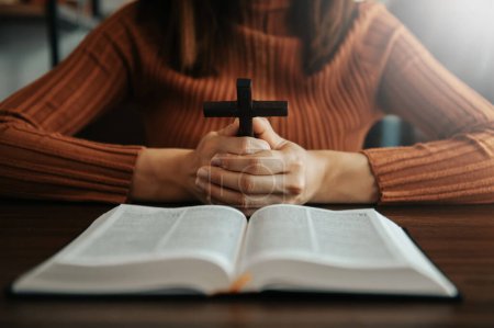 Photo for Woman sitting and studying the scriptures.The  wooden cross in the hands. Christian education concepts The Holy Scriptures open and pray to God - Royalty Free Image