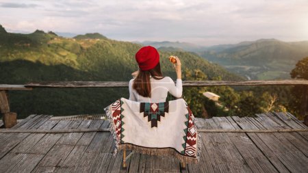 Foto de Rear view image of a female traveler sitting and looking at a beautiful mountain and nature view - Imagen libre de derechos