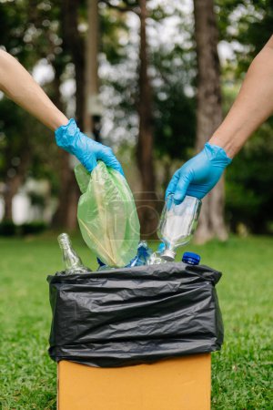 Foto de People hand holding garbage bottle plastic and glass putting into recycle bag .pollution, ecology and plastic concept - Imagen libre de derechos