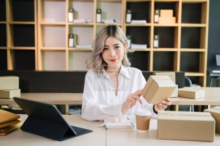 Photo for Startup small business SME, Entrepreneur owner Asian woman using tablet ,taking receive and checking online purchase shopping order to prepare pack product boxes. - Royalty Free Image