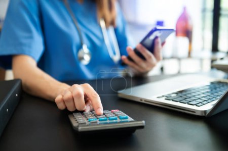 Foto de Healthcare costs and fees concept. smart doctor used a calculator and smartphone, laptop for medical costs in hospital - Imagen libre de derechos