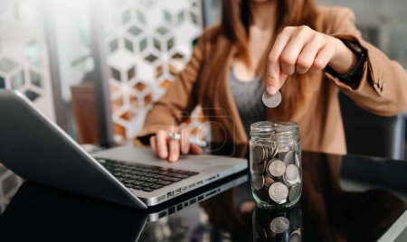 Téléchargez les photos : Businesswoman putting coins in glass with using laptop, concept saving money for finance accounting in office - en image libre de droit