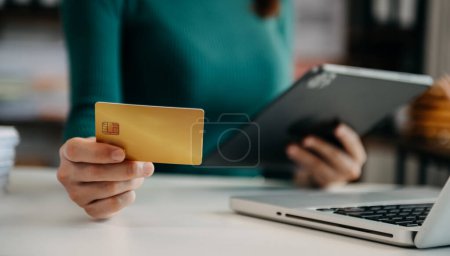 Photo for Woman using credit card for mobile payments online shopping,omni channel,sitting on table,virtual icons graphics interface screen - Royalty Free Image