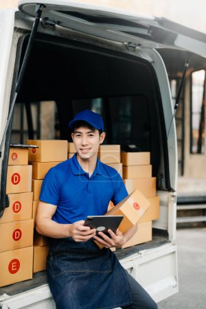 Photo for Smiling delivery man standing in front of his van with Holding Box and tablet delivery home and shipping - Royalty Free Image