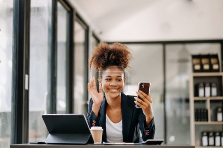 Téléchargez les photos : Femme d'affaires assistant à une vidéoconférence et tenant un smartphone dans un bureau moderne - en image libre de droit