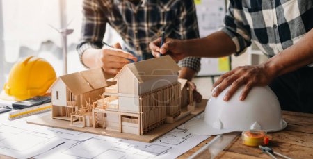 Téléchargez les photos : Maison miniature avec architectes faisant modèle architectural dans le bureau ensemble. pour former un nouveau bâtiment - en image libre de droit