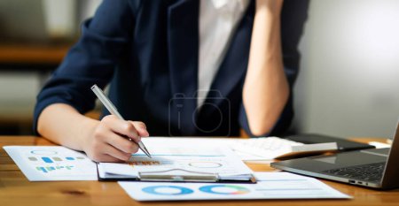 Photo for Businesswoman with documents on office desk with laptop and smartphone and graph business diagram and woman working in morning light - Royalty Free Image