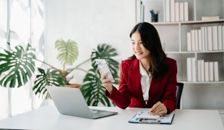 Téléchargez les photos : Femme d'affaires confiante travaillant sur portable ang tenant le téléphone dans le bureau à la maison - en image libre de droit