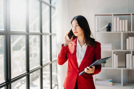 Téléchargez les photos : Asiatique Femme d'affaires Parler au téléphone et utiliser le téléphone au bureau - en image libre de droit