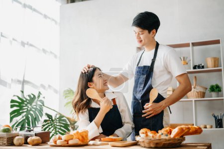 Foto de Amantes de Asia o pareja cocinando en cocina con pan en la mesa. - Imagen libre de derechos