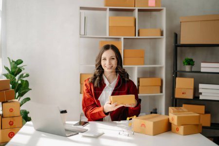 Photo for Startup small business SME, Entrepreneur owner woman using laptop taking receive and checking online purchase shopping order to prepare pack product boxes.  at home office - Royalty Free Image