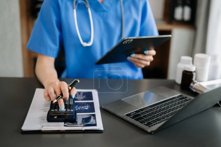Téléchargez les photos : Smart doctor a utilisé une calculatrice et une tablette pour les frais médicaux à l'hôpital - en image libre de droit