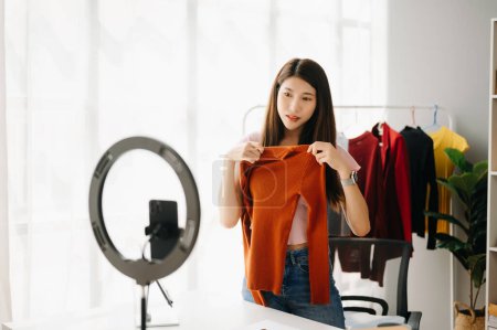 Téléchargez les photos : Concept de blogueur de mode, Jeune femme asiatique vendant des vêtements sur vidéo streaming.Startup PME de petite entreprise, en utilisant smartphone prendre recevoir et vérifier au bureau - en image libre de droit