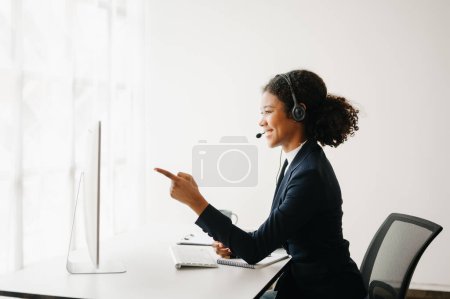 Photo for Serious call center operator in wireless headset talking with customer, African woman in headphones with microphone consulting client on phone in customer support service in business center - Royalty Free Image