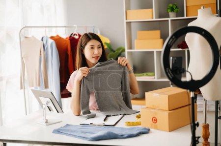Photo for Fashion blogger concept, Young Asian woman selling clothes on video streaming.Startup small business SME, using smartphone and tablet taking receive and checking in office - Royalty Free Image