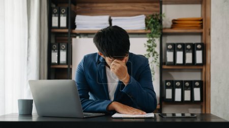 Téléchargez les photos : Frustré jeune homme d'affaires travaillant sur un ordinateur portable assis à son lieu de travail dans un bureau moderne - en image libre de droit