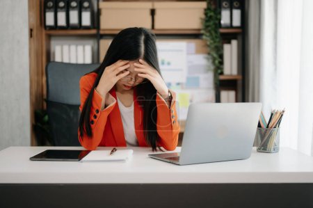 Foto de Mujer asiática sensación migraña cabeza strain.Overworked financiero mujer de negocios con en el ordenador portátil en la oficina moderna. - Imagen libre de derechos