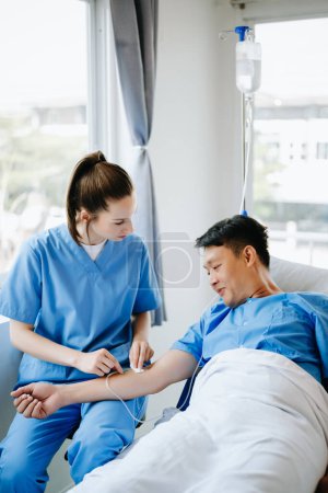 Photo for Friendly Female  Nurse Making Rounds does Checkup on Patient Resting in Bed. She Checks drip while Man Fully Recovering after Successful Surgery in hospital - Royalty Free Image