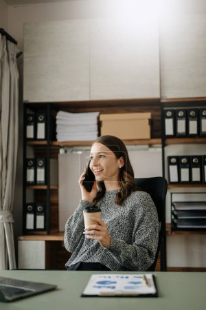Foto de Mujer trabajadora o gerente femenino sosteniendo teléfono inteligente y café en la oficina moderna - Imagen libre de derechos