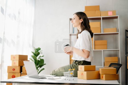 Photo for Startup small business SME, Entrepreneur owner woman using laptop taking receive and checking online purchase shopping order to preparing pack product boxes.  at home office - Royalty Free Image
