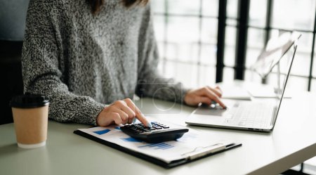 Téléchargez les photos : Gros plan de la femme d'affaires ou comptable avec ordinateur portable, calculer sur le bureau sur le coût au bureau à domicile. - en image libre de droit