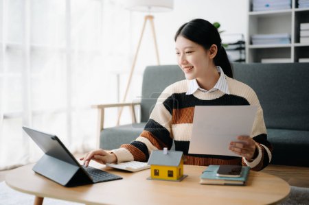 Téléchargez les photos : Jeune agent immobilier travailleur travaillant avec tablette à table dans le bureau à domicile et petite maison - en image libre de droit