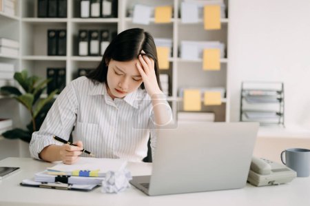 Téléchargez les photos : Femme asiatique se sentant migraine tête tendue.Overworked femme d'affaires financière tout en travaillant sur ordinateur portable au bureau. - en image libre de droit