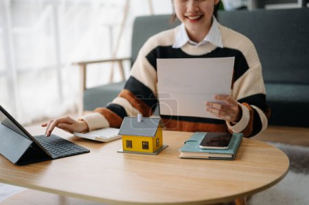 Téléchargez les photos : Jeune agent immobilier travailleur travaillant avec tablette à table dans le bureau à domicile et petite maison - en image libre de droit