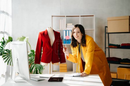 Téléchargez les photos : Créatrice de mode femme avec tablette numérique dans un studio moderne avec des vêtements - en image libre de droit