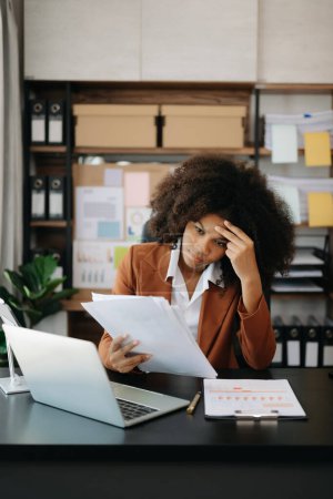 Foto de La mujer de negocios africana está estresada, aburrida y pensando demasiado en trabajar en la computadora portátil en la oficina moderna - Imagen libre de derechos
