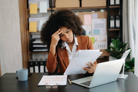 Téléchargez les photos : Femme d'affaires africaine est stressée, ennuyée et trop réfléchie de travailler sur un ordinateur portable au bureau moderne - en image libre de droit