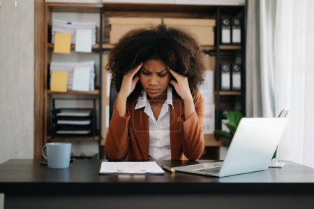 Foto de La mujer de negocios africana está estresada, aburrida y pensando demasiado en trabajar en la computadora portátil en la oficina moderna - Imagen libre de derechos